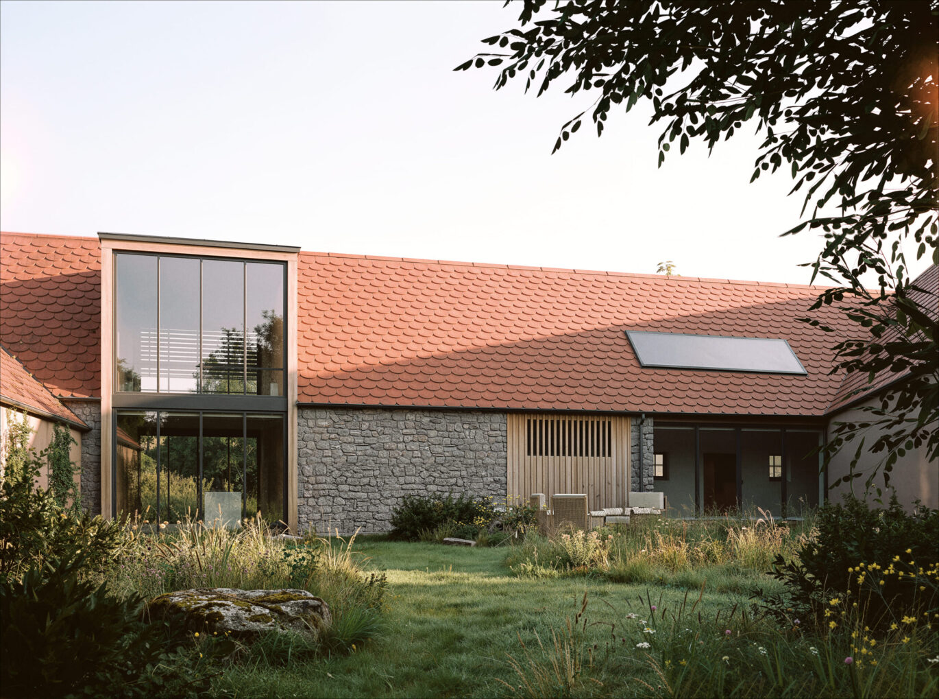 Pohled ze zahrady na rodinný dům Tálín s kamennou zdí a vloženým proskleným blokem přes dvě podlaží, návrh od architektů z MA Studia