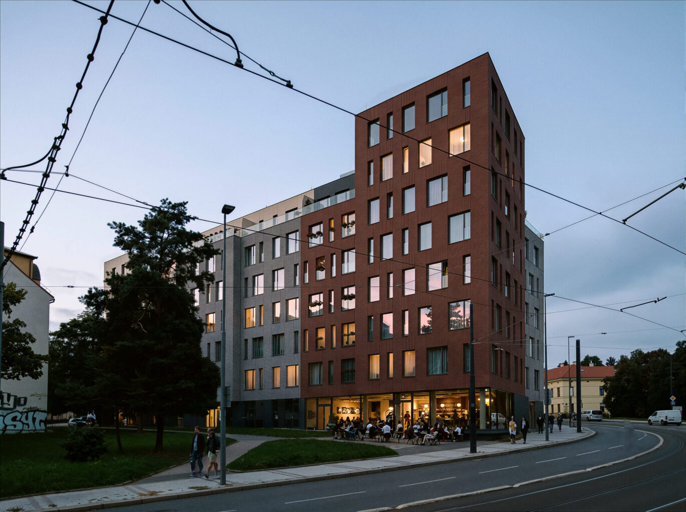 Bytový dům v pražské Libni za soumraku, rozsvícený komerční parter s kavárnou na nároží, návrh od archiektů z MA Studia